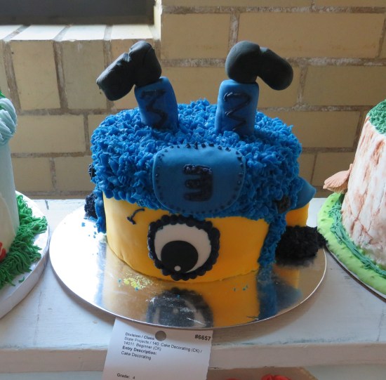 Yellow cake with blue top, Minion sticking out of it, and a single big eye on the bottom.