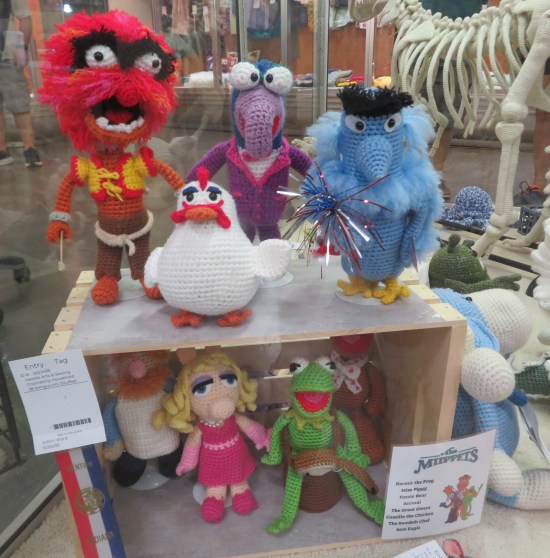 Eight Muppets crocheted, displayed in a crate -- four inside, four on top.