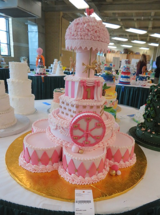 giant pink cake with merry-go-round animals on top, all on top of several smaller pink cakes shaped faintly like snare drums.