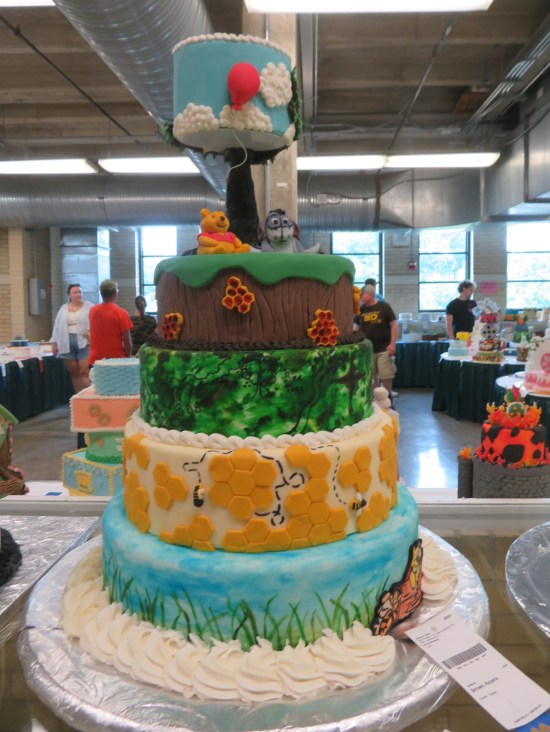 5-layer cake with various Pooh elements including beehive honeycombs and a red balloon on the fifth layer.