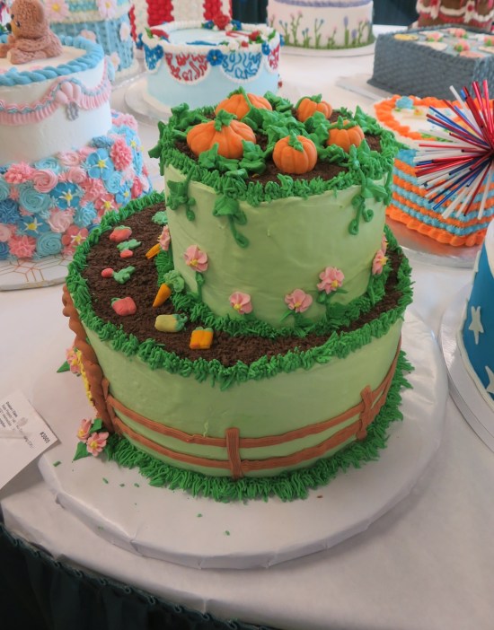 Two-layer cake with icing pumpkins on top and an icing fence around the base.