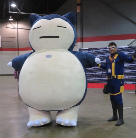 Giant Snorlax costume next to a normal-sized Cyclops cosplayer. Both have arms outstretched.