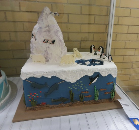 Rectangular cake decorated like ocean with penguins and narwhals frolicking in the water. Toppers are an iceberg, penguins and polar bears.