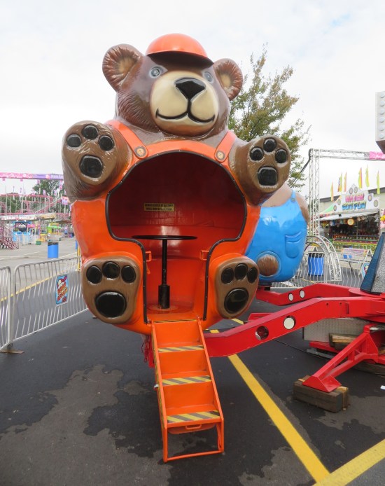 Spinning ride with the seats designed like a happy bear dressed in a orange handyman uniform.