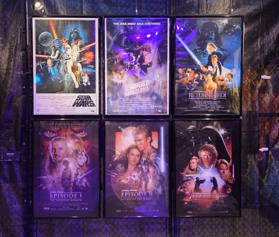Posters for the first six Star Wars films on a chain-link wall.