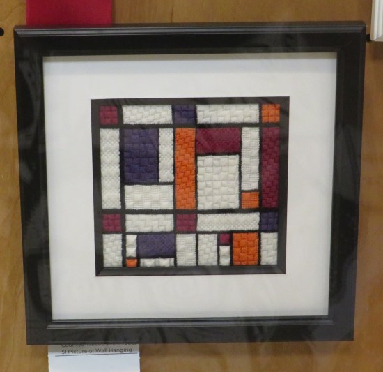 Small framed needlework resembling a Piet Mondrian abstract painting.