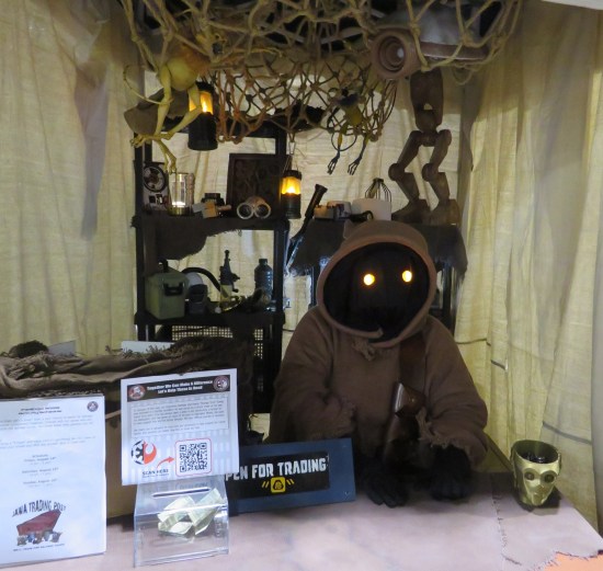 Jawa cosplayer sitting in a sand-colored tent with a sign: "Open for Trading".