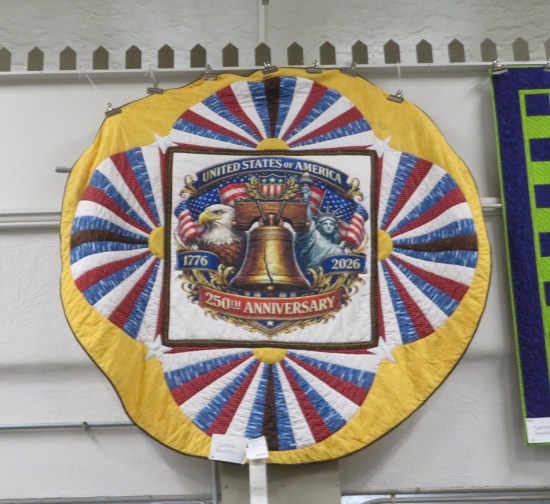 round yellow hanging quilt with picture of the Liberty bell reading "United States of America 250th anniversary 1776-2026".