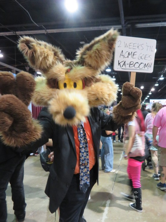 big furry Wile E. Coyote cosplayer carrying sign: "2 Weeks Till Acme Goes Ka-Boom!"