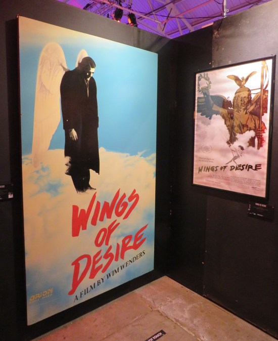 Black walled corner with Wings of Desire movie poster and large painting of a winged Bruno Ganz above the logo.