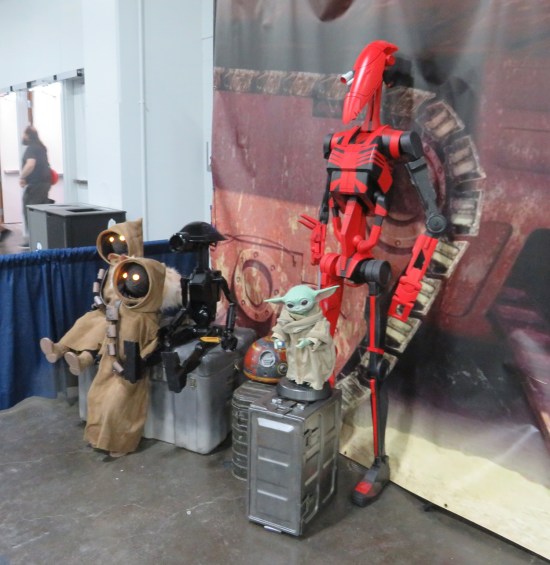 Star Wars stuff including Baby Yoda, red and black Battle Droid, two Jawas and a black Pit Droid, against a Jawa Sandcrawler backdrop.