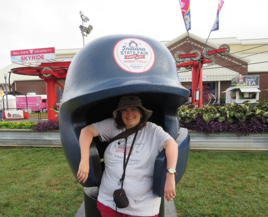 Anne posing inside a baseball training helmet large enough to envelop her entire upper torso.