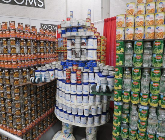Can sculpture of Stay-Puft Marshmallow Man lumbering between canned skyscrapers.