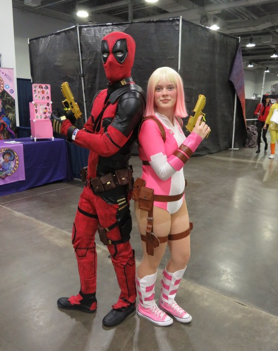 Deadpool and Gwenpool cosplayers, both armed and back-to-back.