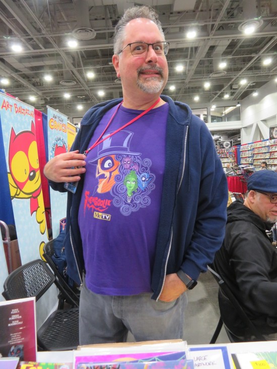 Franco Aureliani at his booth wearing a purple Svengoolie shirt he designed himself.