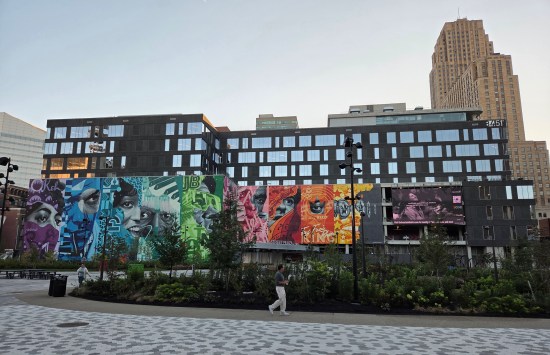 Parking garage with mural behind a lush city park. One jogger runs by.
