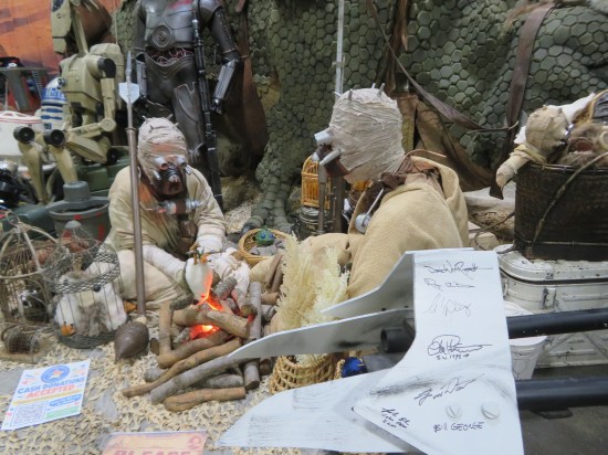 Life-size diorama of Tusken Raider nuclear family sitting around an unlit campfire.