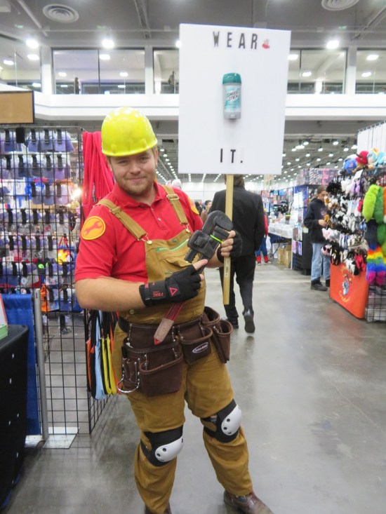 costume of a Team Fortress 2 Engineer carrying a picket sign with a Speed Stick bottle glued to it and the message "WEAR IT".