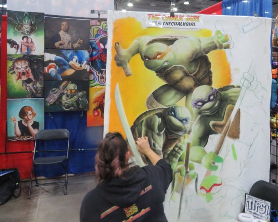 Chalk artist works on large TMNT piece at her comic-con booth.