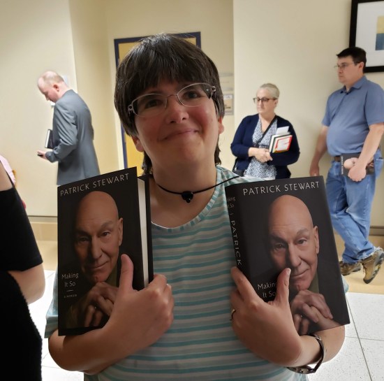 Anne smiling and holding up two copies of Patrick Stewart's memoir.