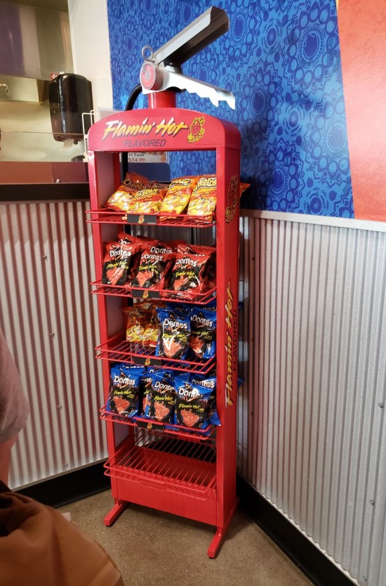 Five-foot fire extinguisher shaped red shelf. Several bags of chips are for sale.