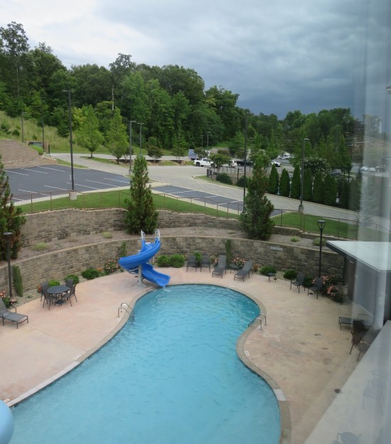 Bird's-eye view of a pool in a hotel backyard. Beyond are forested mountains and brewing storm clouds.
