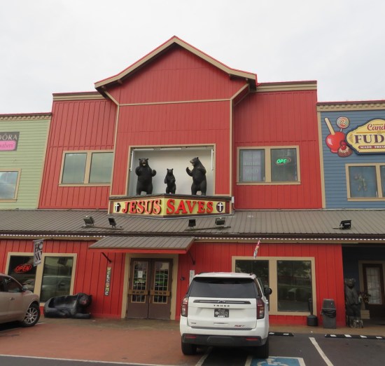 Red general store with a sign that says "JESUS SAVES". Standing on it are statues of Papa, Mama and Baby Bear.