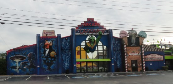 Lazerport Arcade blue building with pics of evil alien, green Ultraman knockoff, strong human golfer and random lightning.