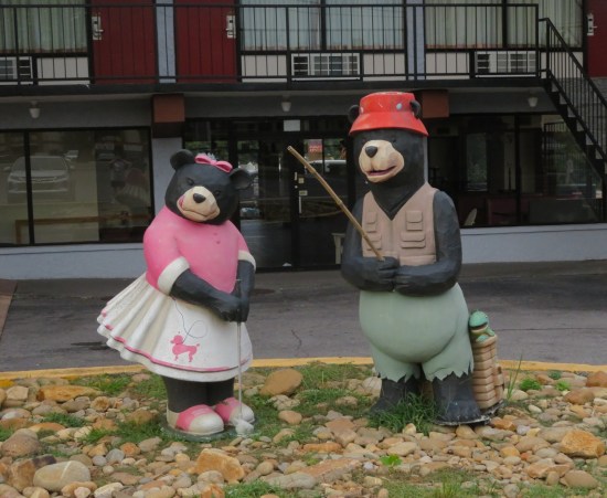 Small bear statues, one dressed as a fisherman and the other as a 1950s school dancer, both in front of a motel.