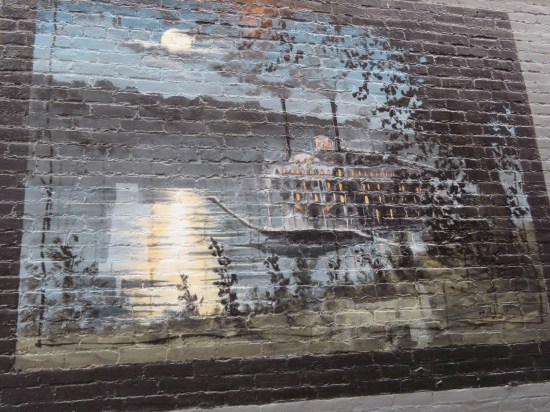 Mural on dark alley bricks of a riverboat at night.