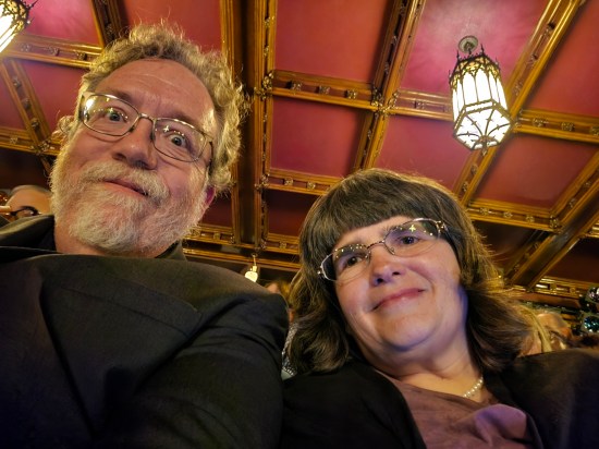Us smiling, nicely dressed and in cramped seats with an old red ceiling and dangling light above us.