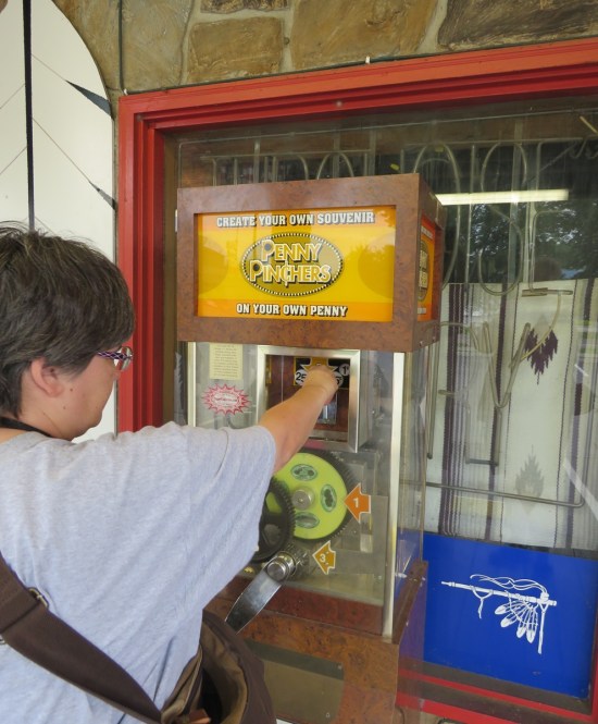 Anne using a smashed penny machine outside a jewelry shop with stone walls.