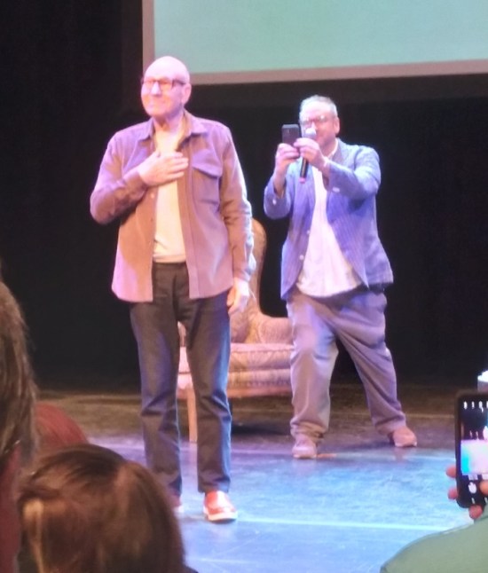 Blurry pic of Patrick Stewart with hand over chest on a stage, while the introducer photographs his back for some reason.