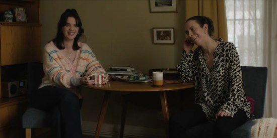 Two thirtysomething women laugh and have tea at a round dinner table.