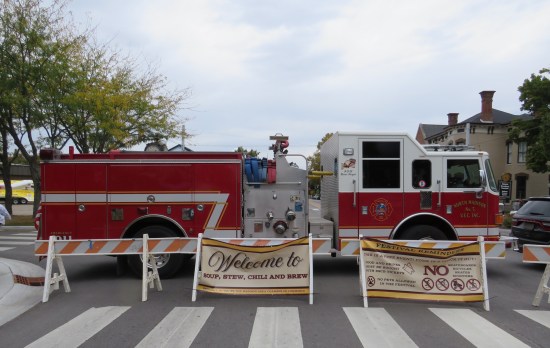Fire truck parked in front of intersection with festival sign leaning against it.