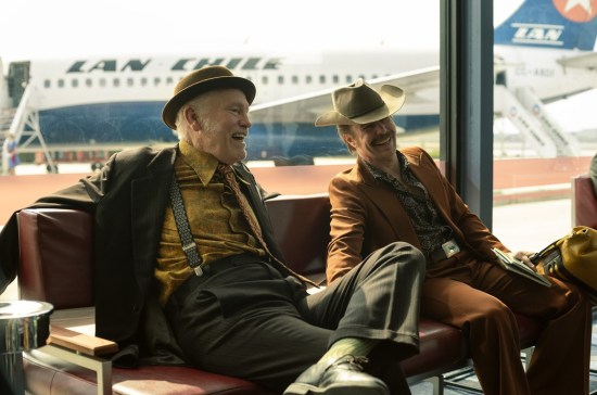 John Malkovich and Sam Rockwell as 1970s guys in awful brown suits and old hats, laughing in an airport.
